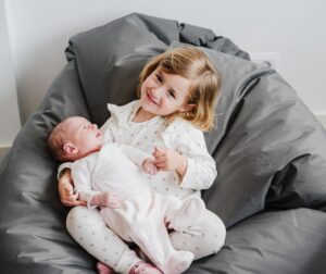 toddler girl sitting on a bean bag holding baby 